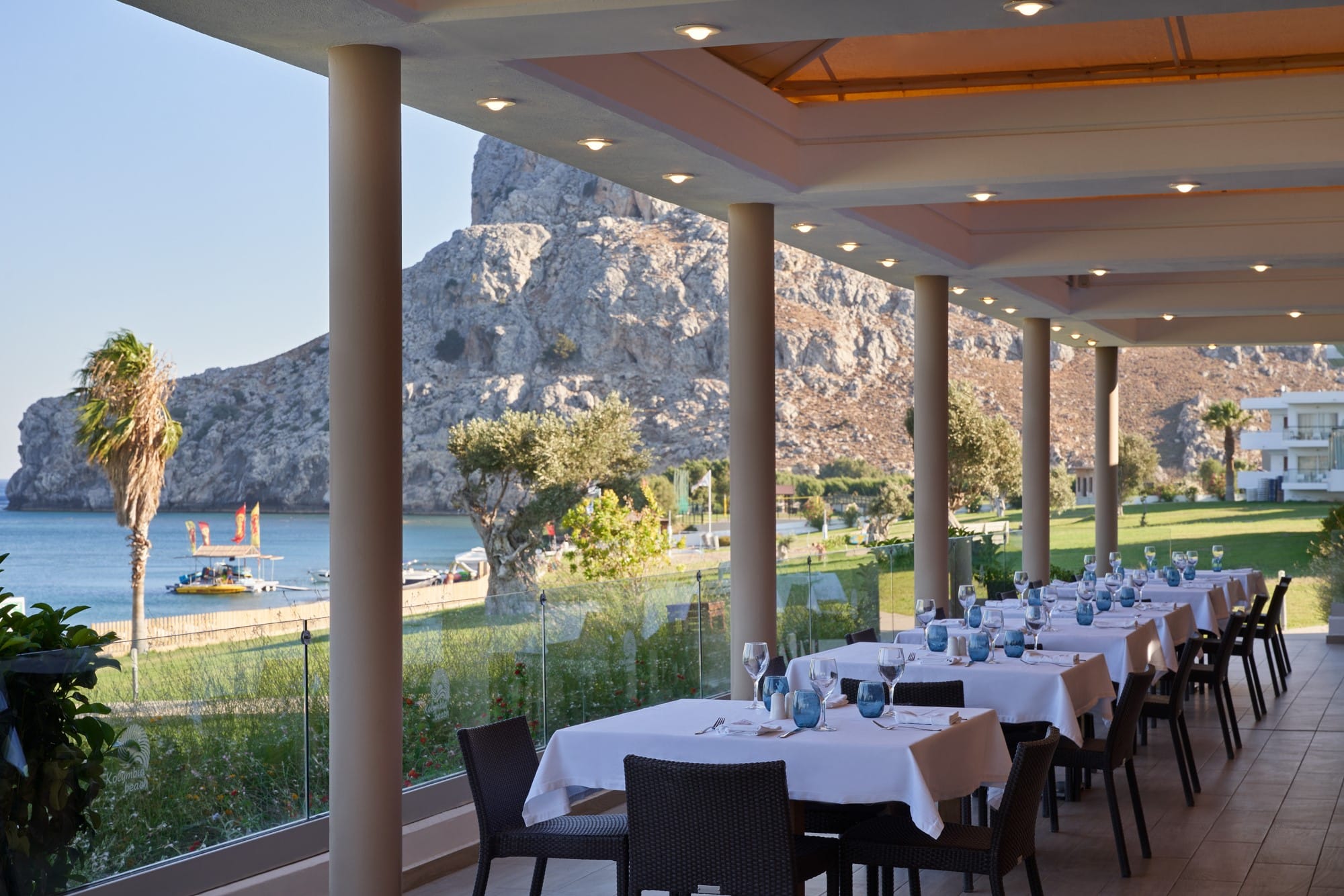 a patio with tables and chairs and a body of water in the background