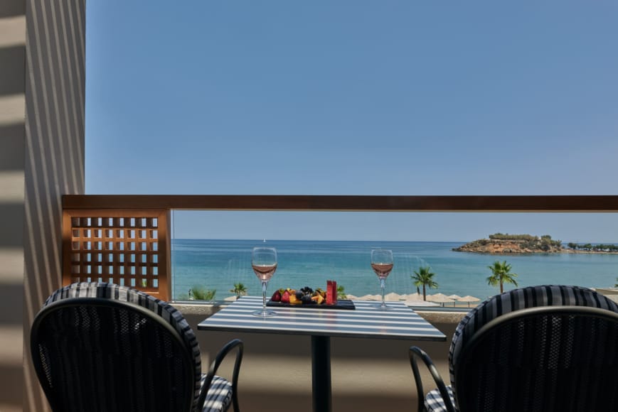 a table with glasses and a drink on it by a window with a view of the ocean