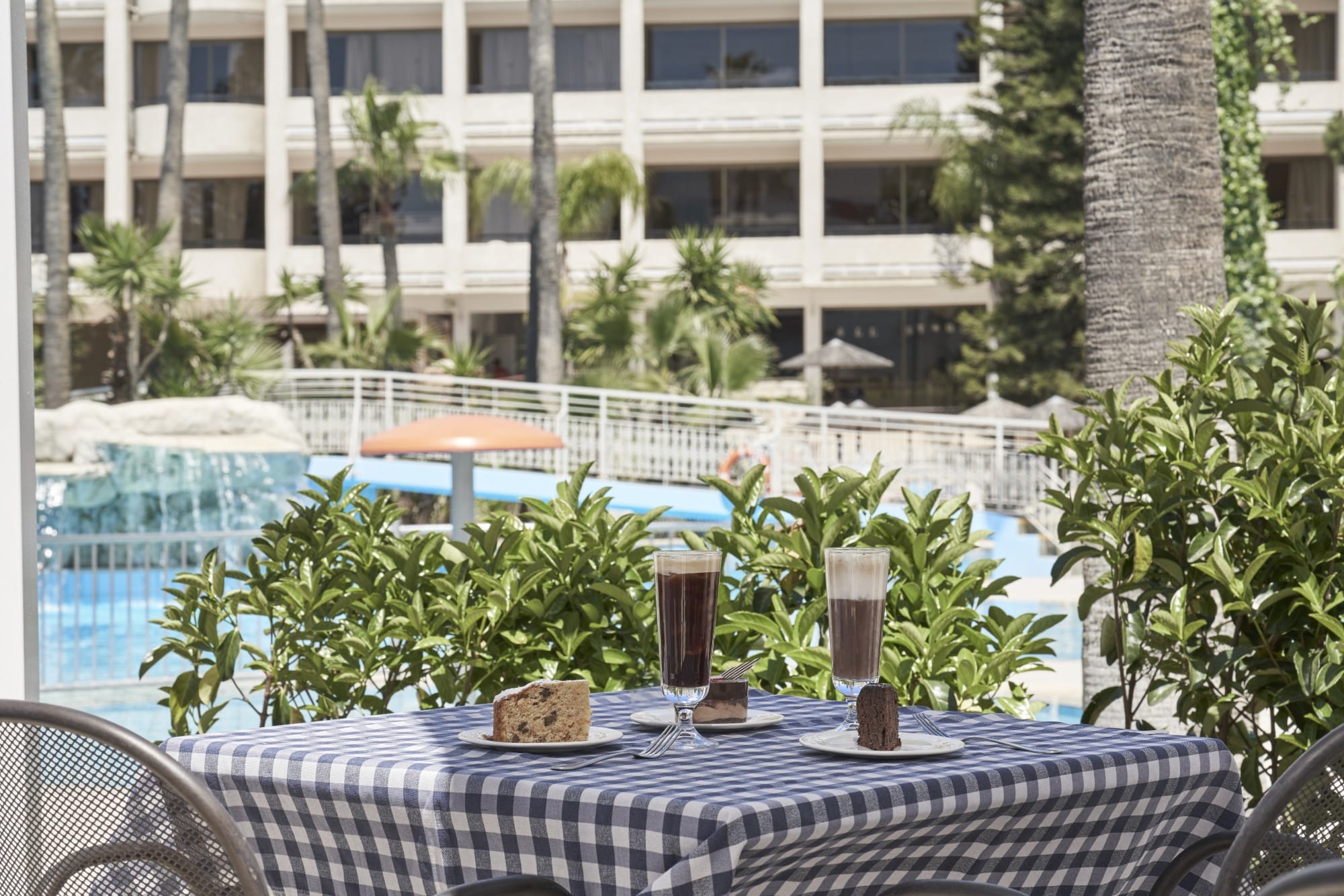 Poolside Dining Area At Atlantica Oasis Hotel In Limassol With Drinks And Lush Greenery