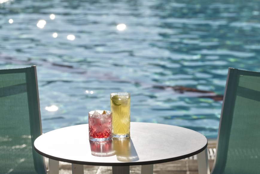 a table with a glass of liquid on it by a body of water