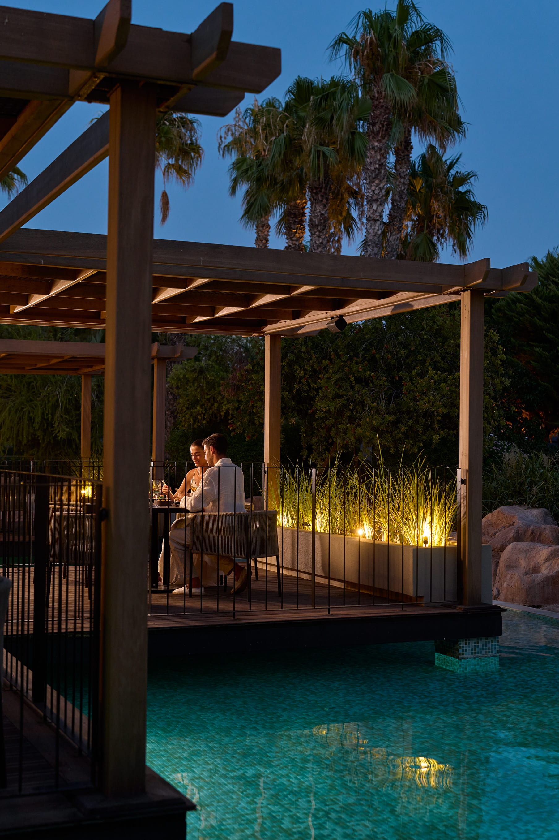 a couple sitting on a bench by a pool