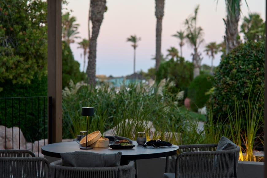 a table with plates and glasses on it by trees and a fence