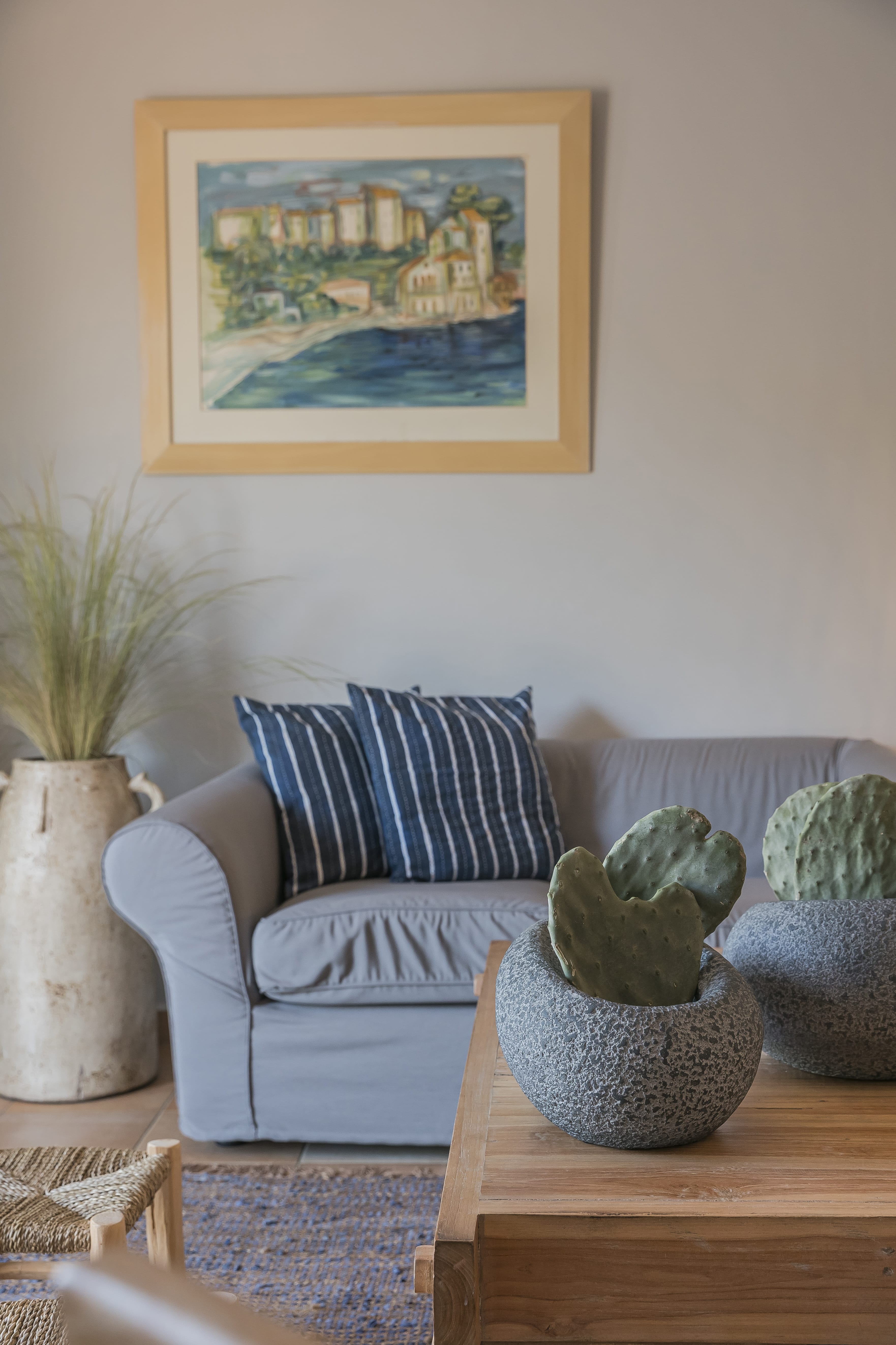 a white couch with a blue and white striped pillow and a painting on the wall