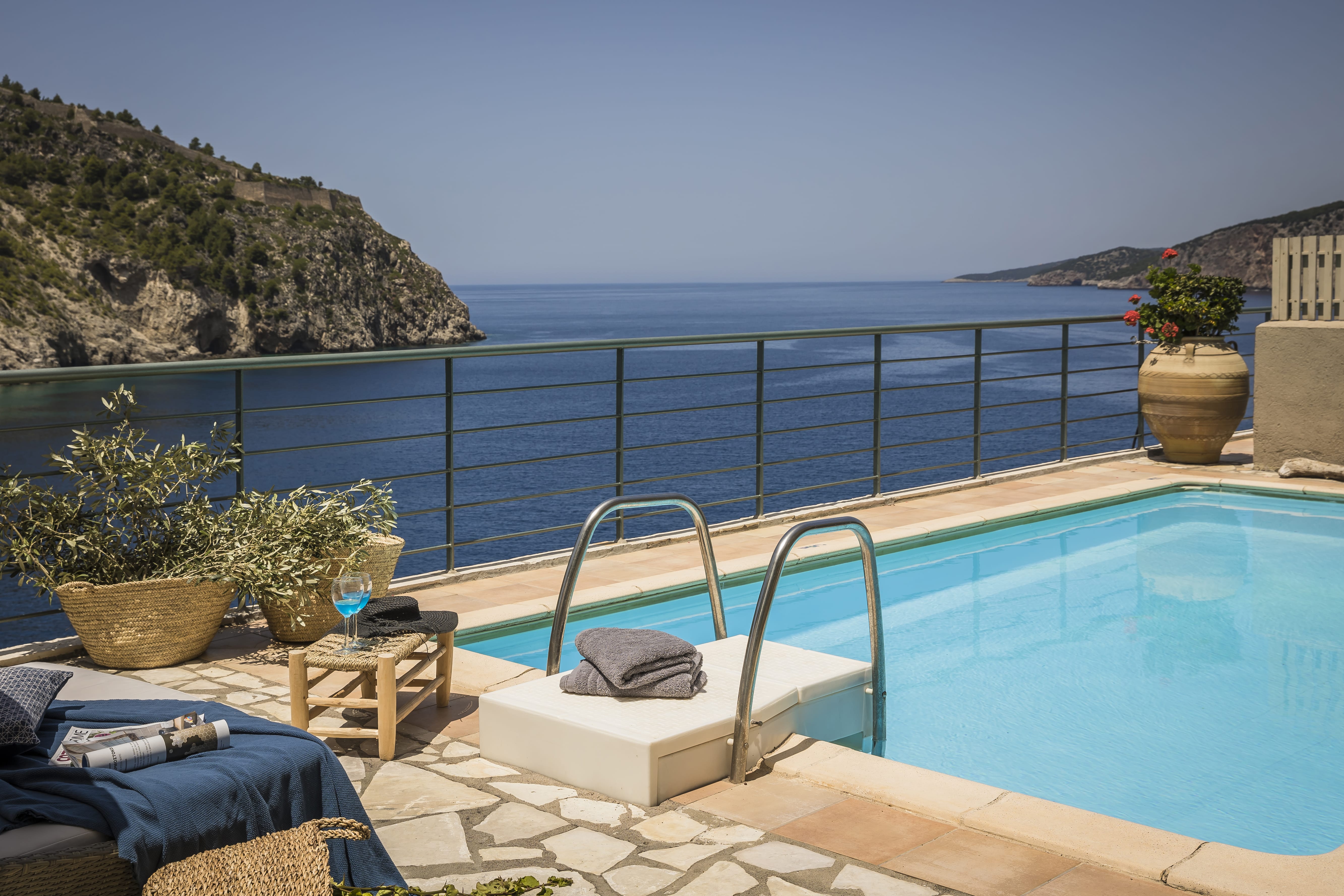 a pool with a deck and chairs by it and a body of water in the background