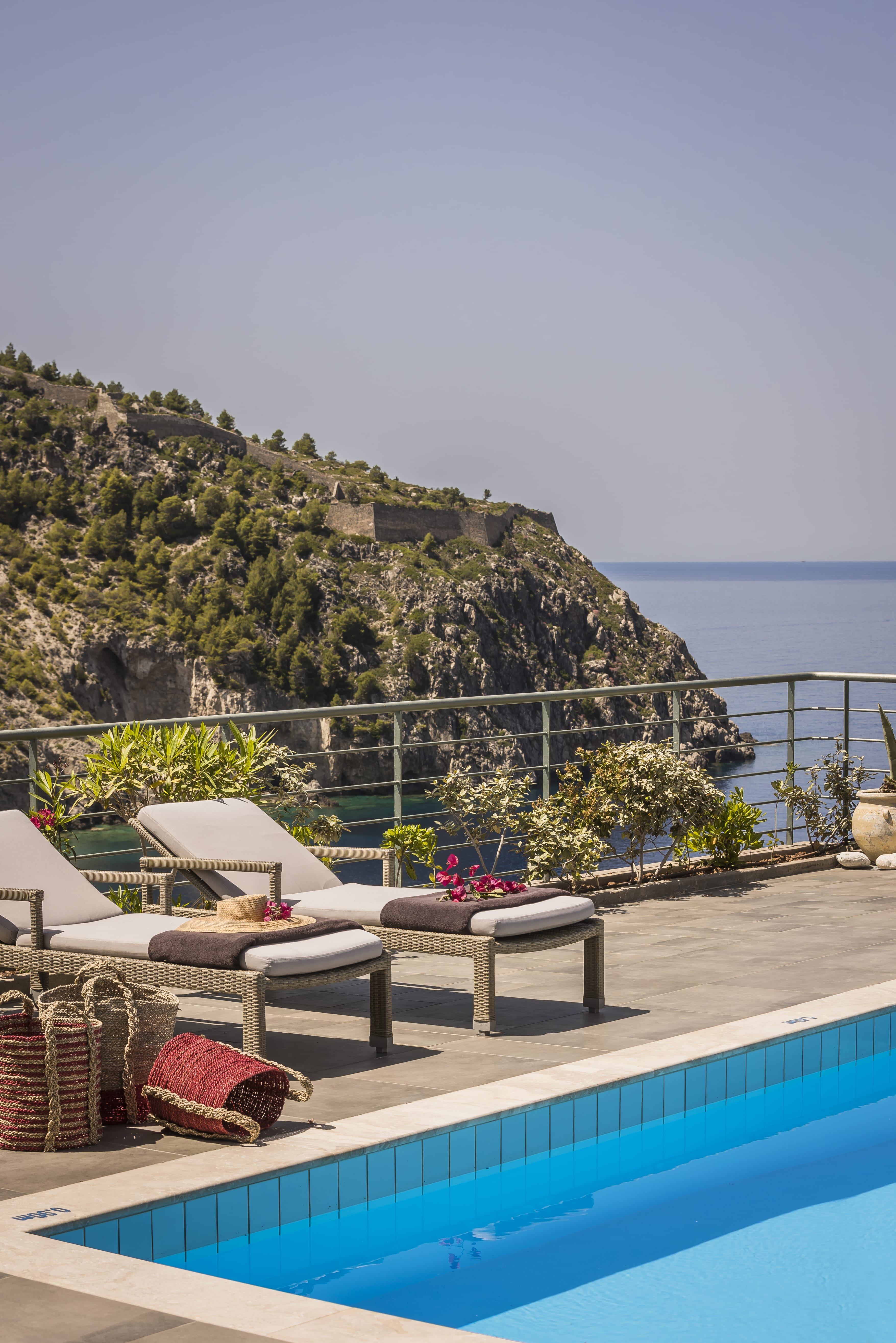 a deck with a pool and a hill with trees and a body of water