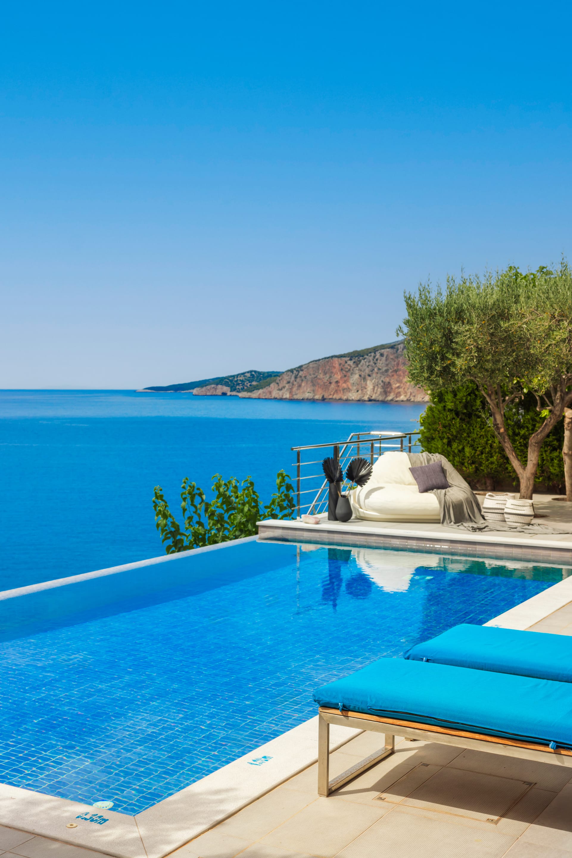a pool with a lounge chair and a deck with a tree and a hill in the background
