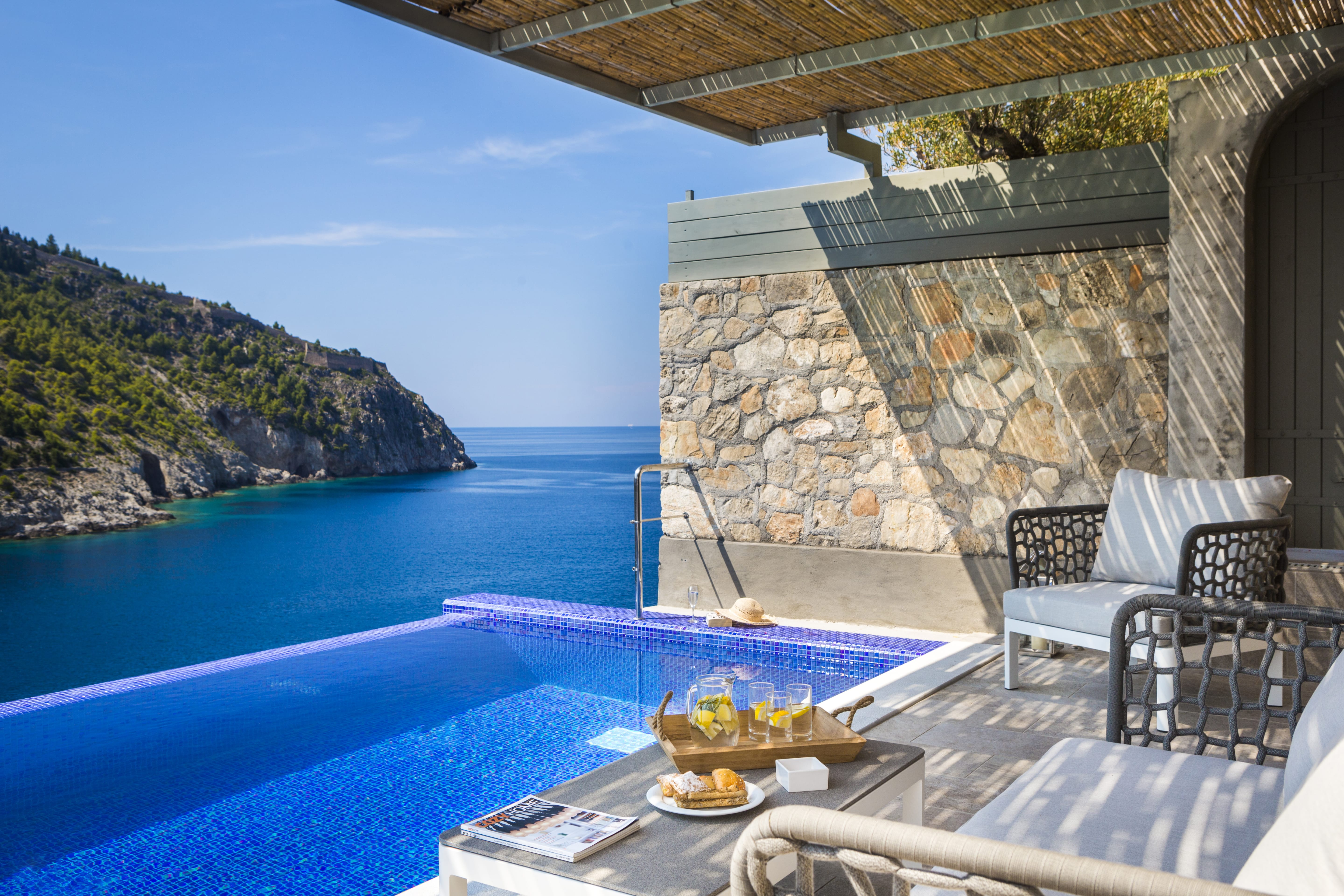 a pool with chairs and a table by it with a stone building in the background
