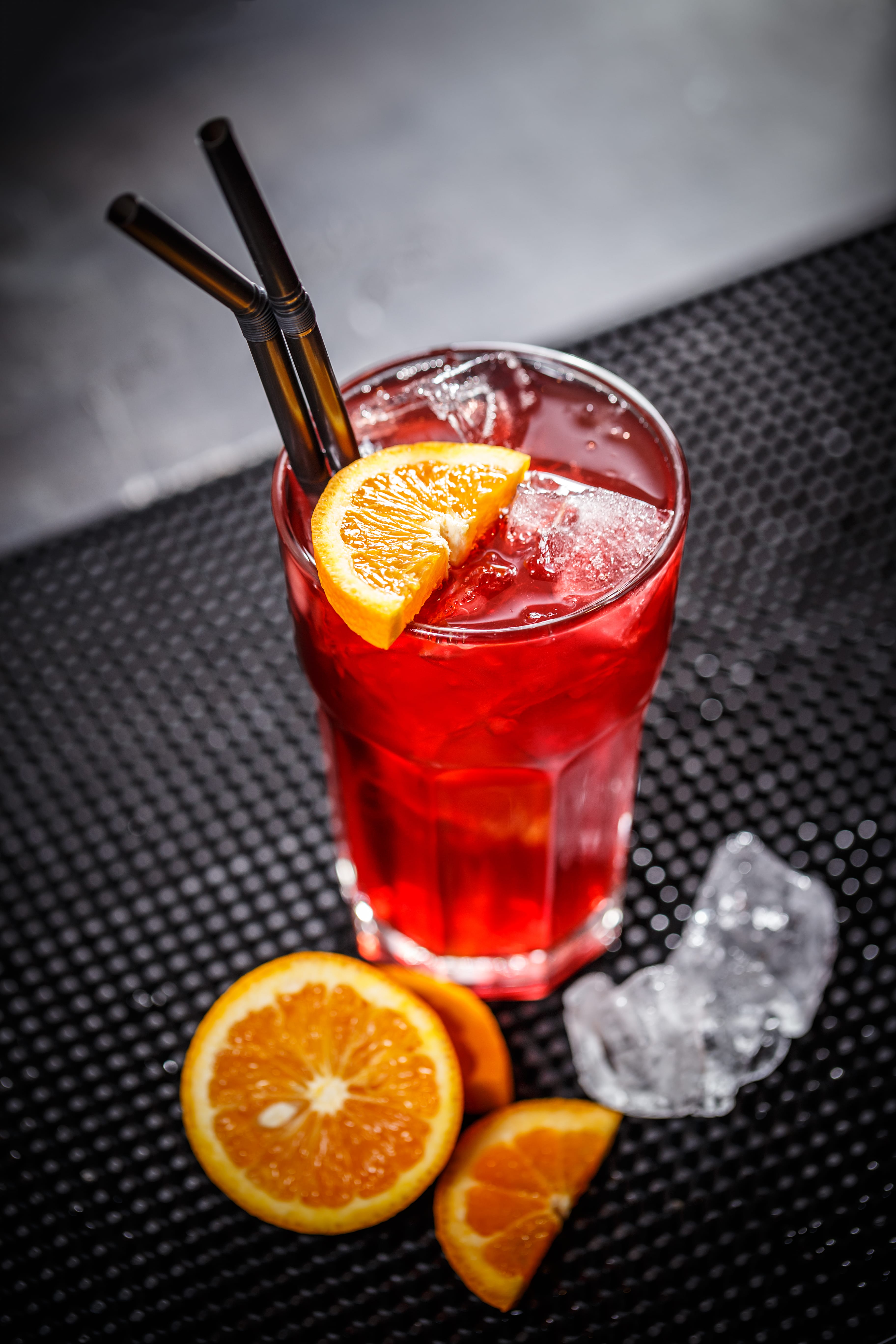 a glass of red liquid with oranges and a spoon