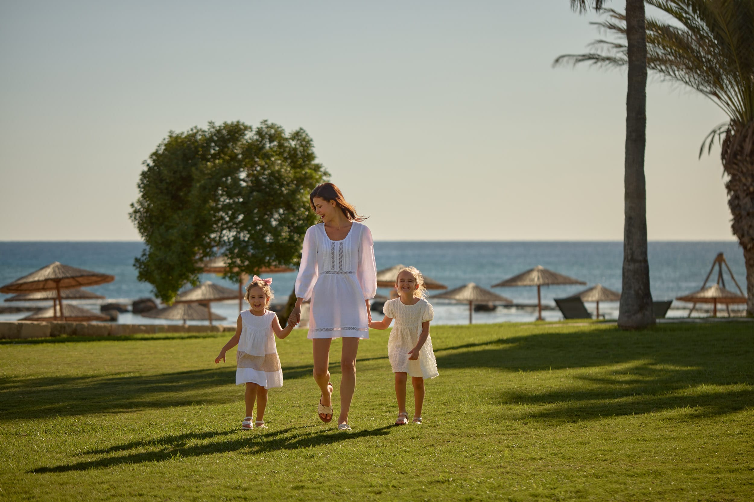 a person and two children walking on a grass field by the water