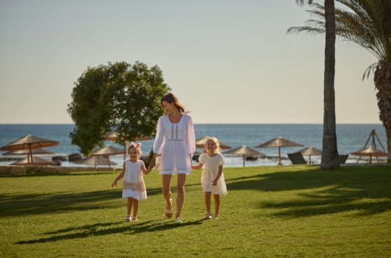 a person and two children walking on a grass field by the water
