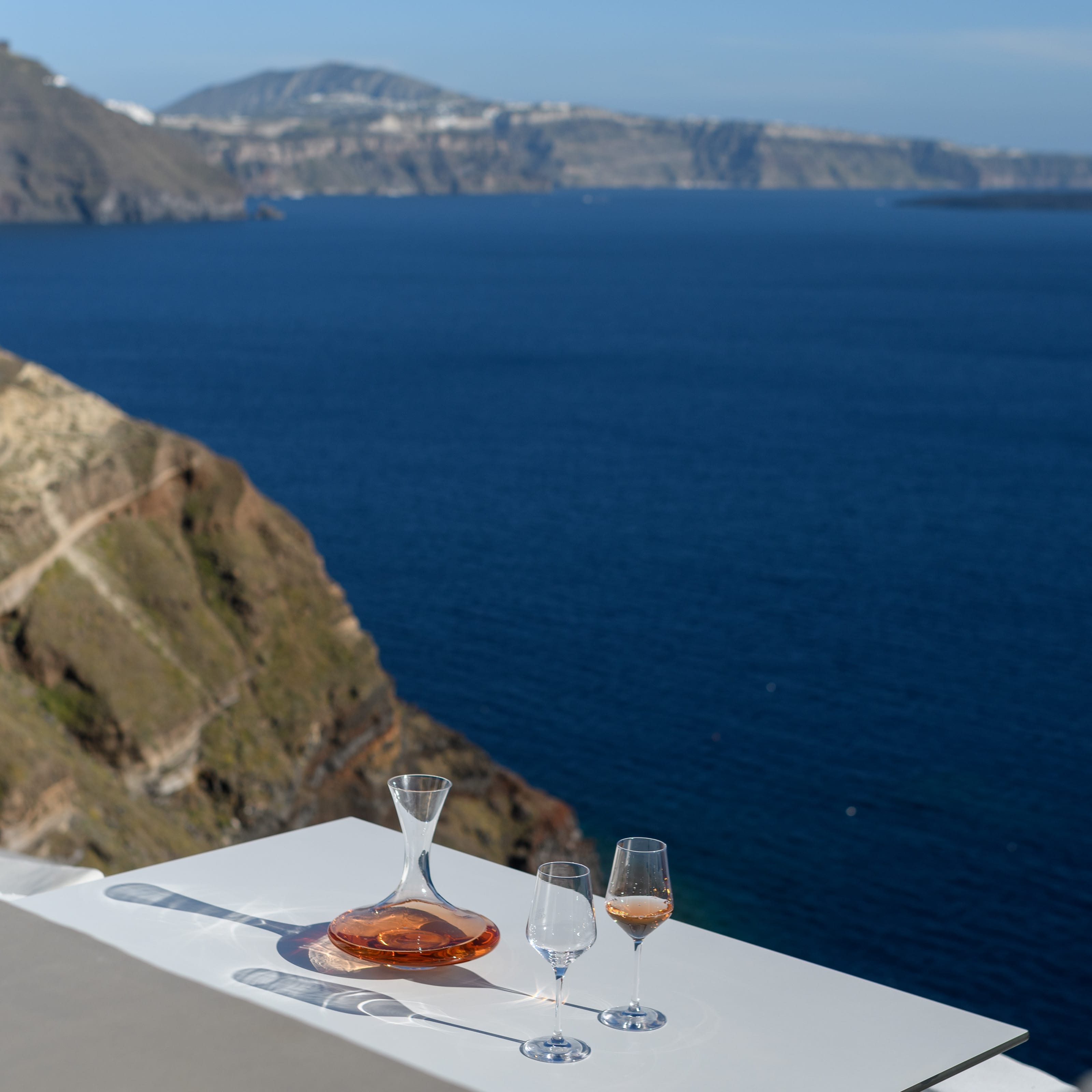 a table with glasses and a plate of food on it by a body of water