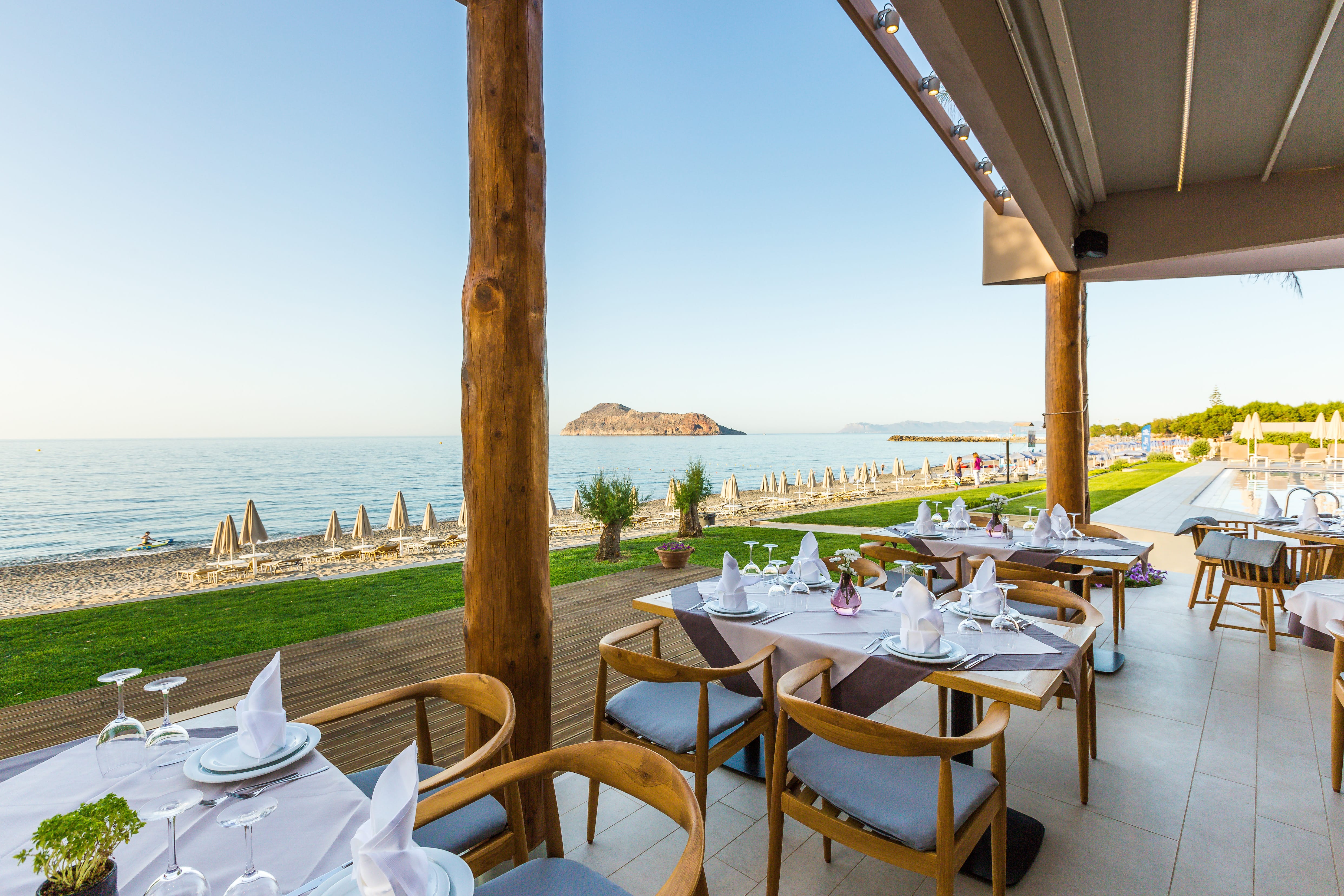 a patio with tables and chairs and a body of water in the background