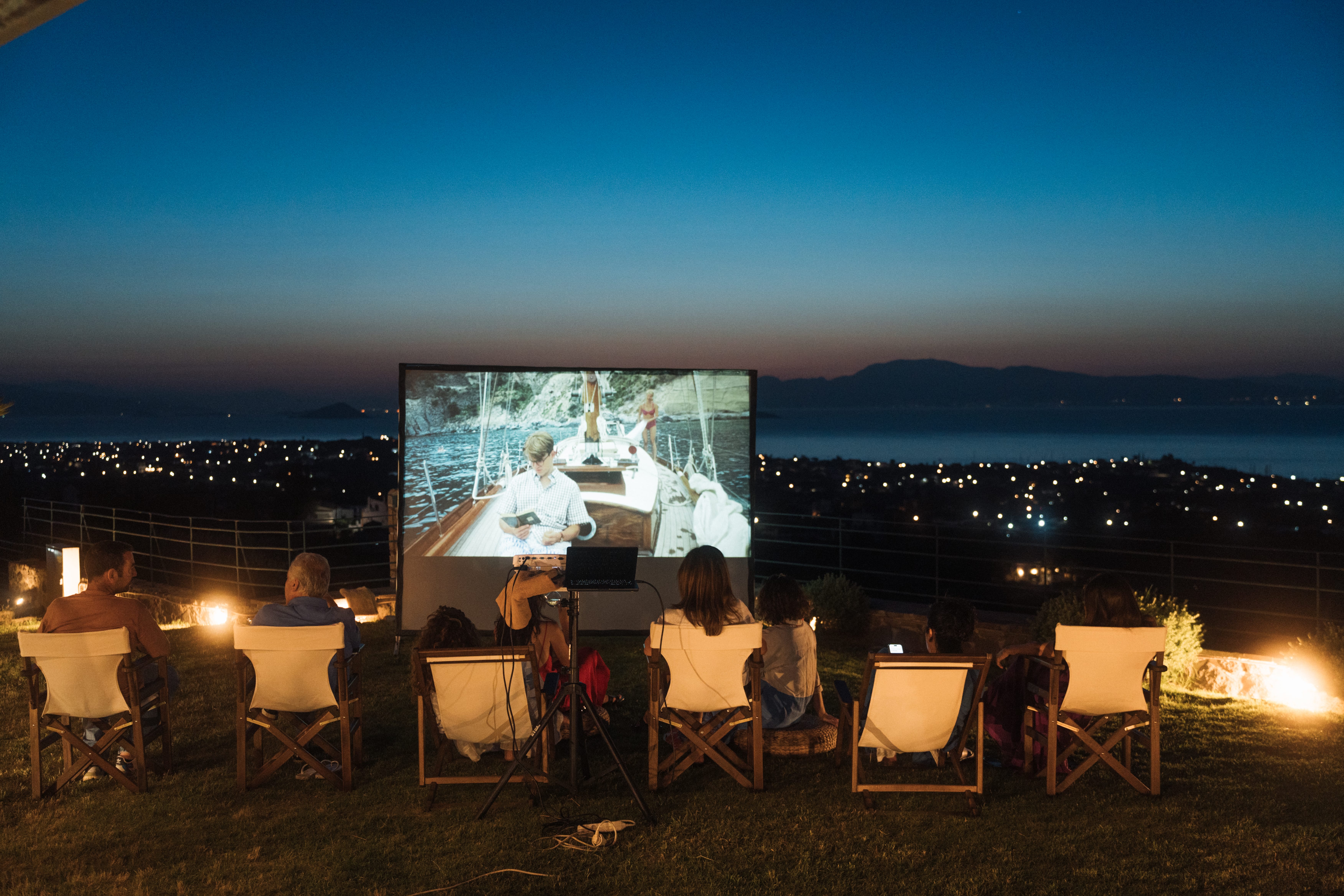 a group of people sitting at a table with a large screen in the background
