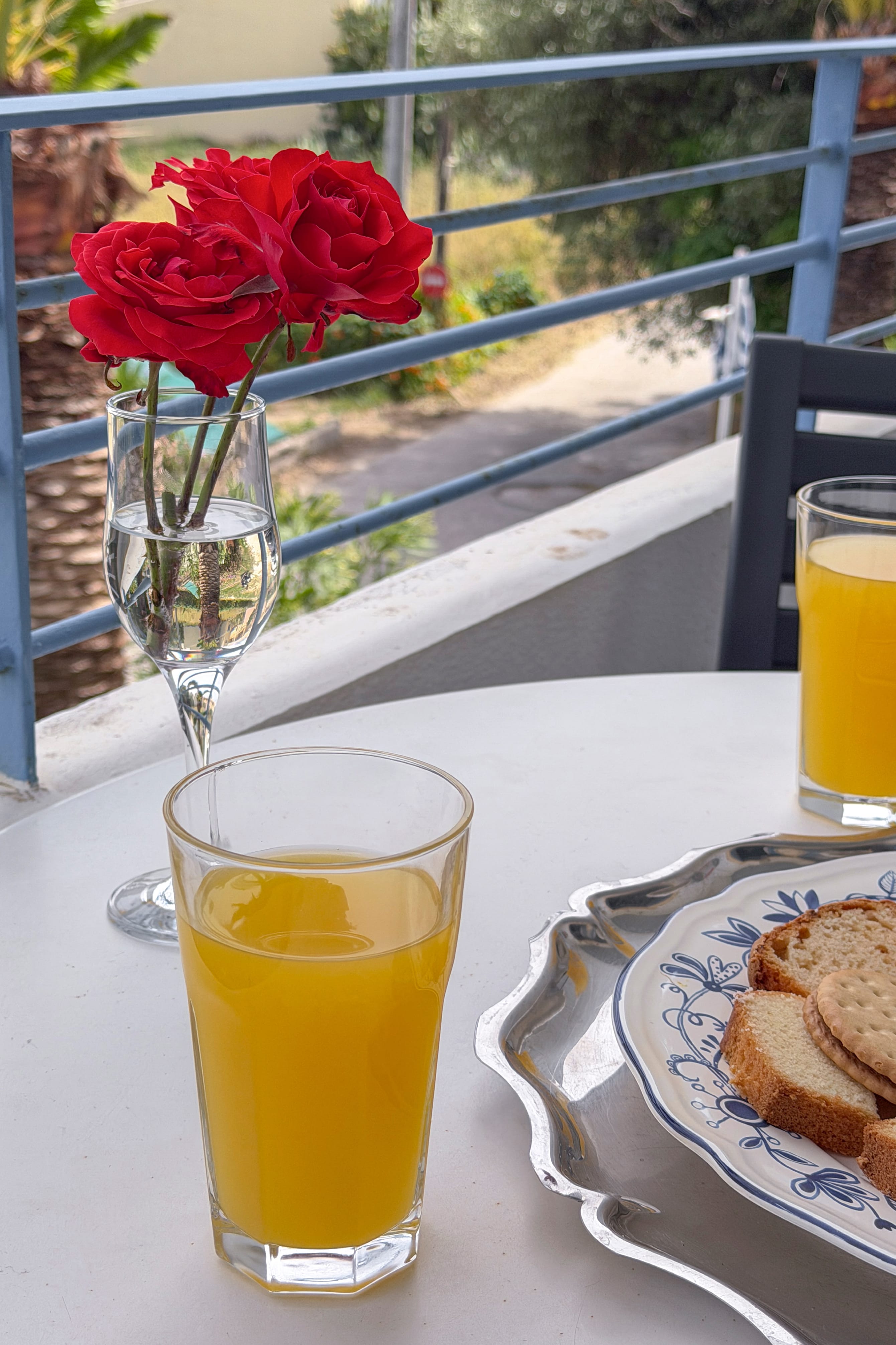a plate of bread and orange juice on a table with a glass of orange juice and a vase of roses