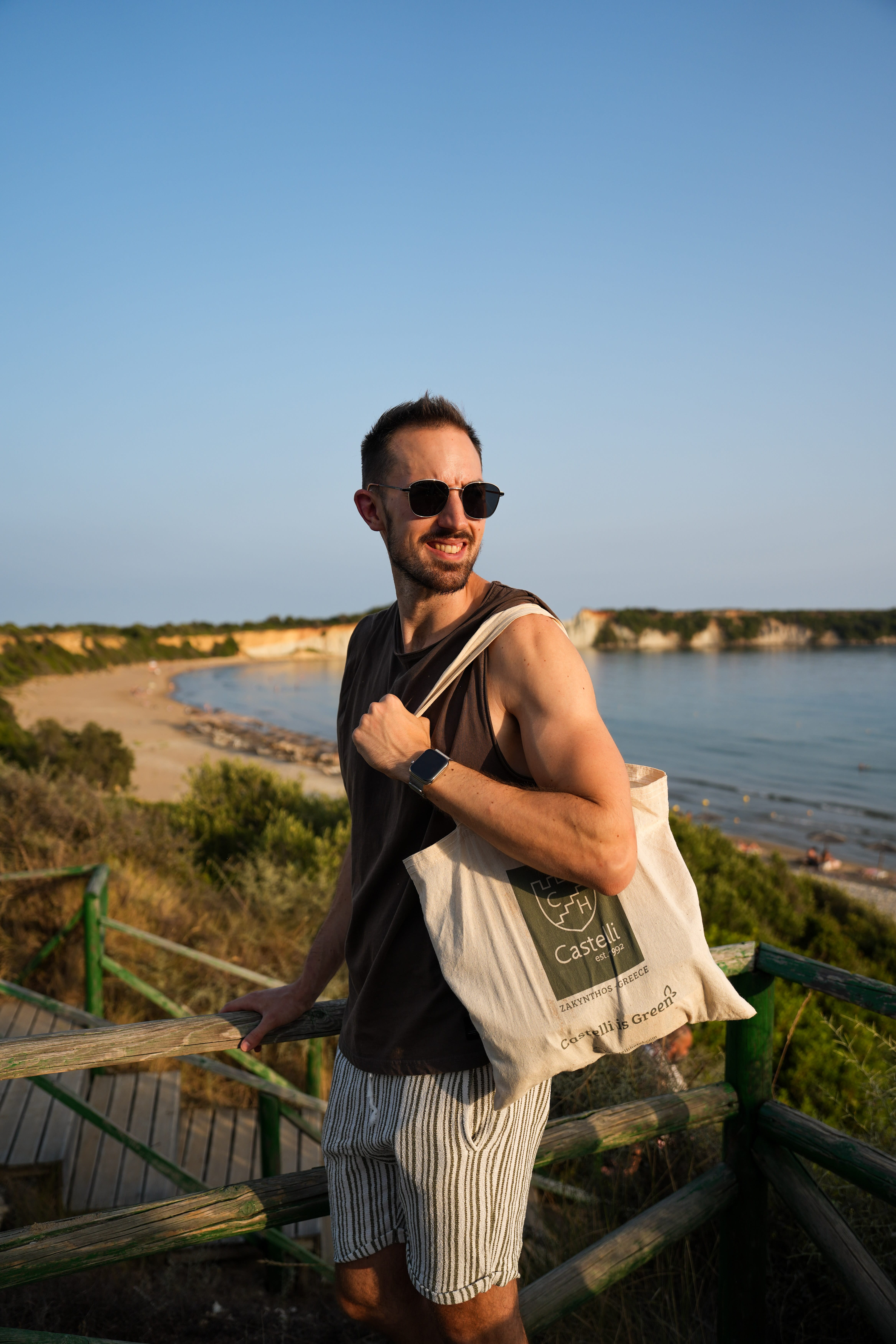 a man leaning on a railing with water and a beach in the background