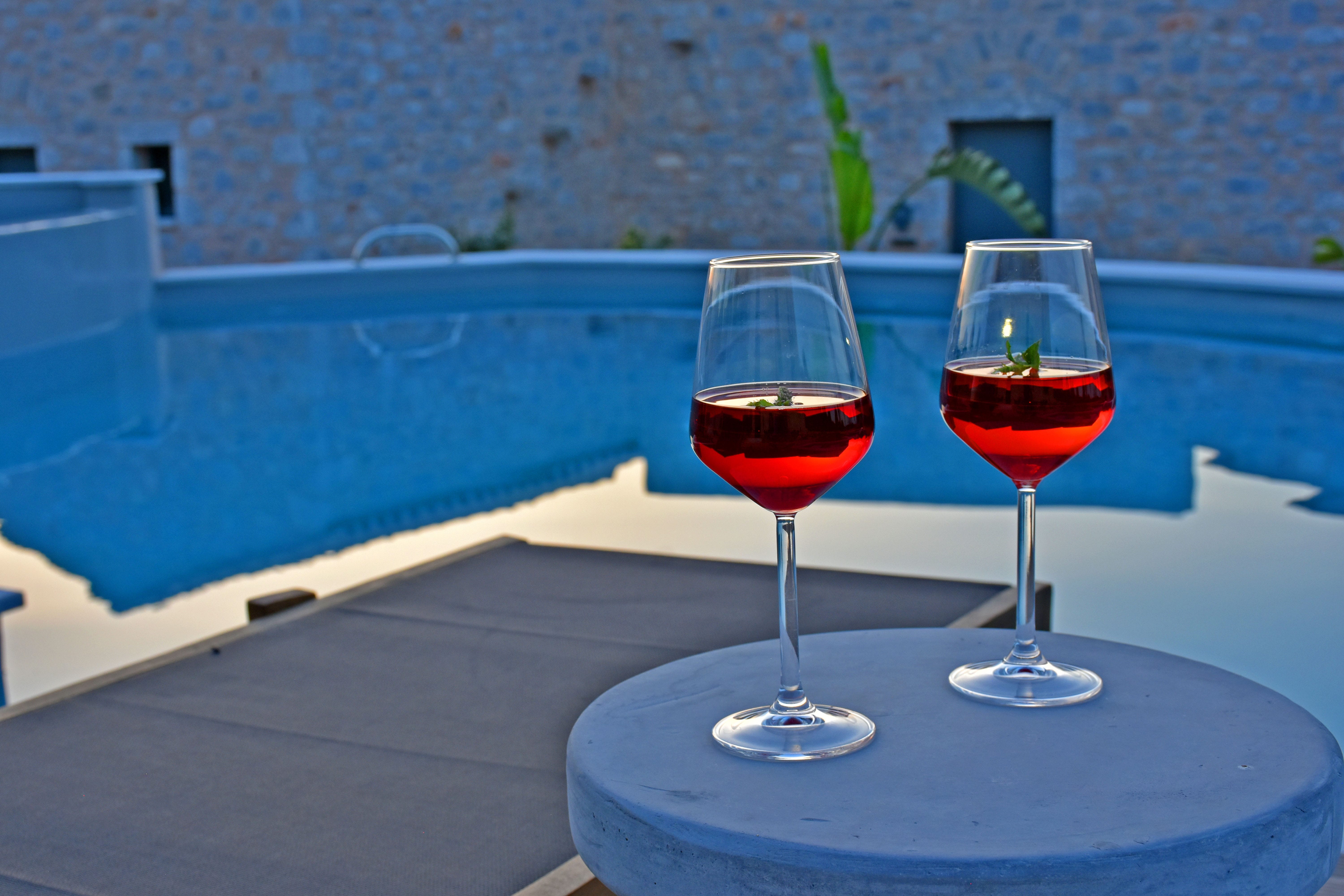 two glasses of red wine on a table by a pool