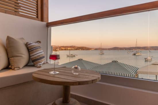 a table with a glass of wine on it by a window with a view of the water and