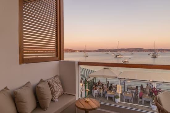 a room with a view of the ocean and a deck with chairs