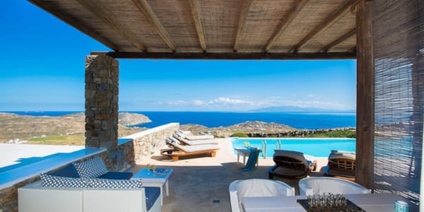 a deck with chairs and tables and a body of water in the background