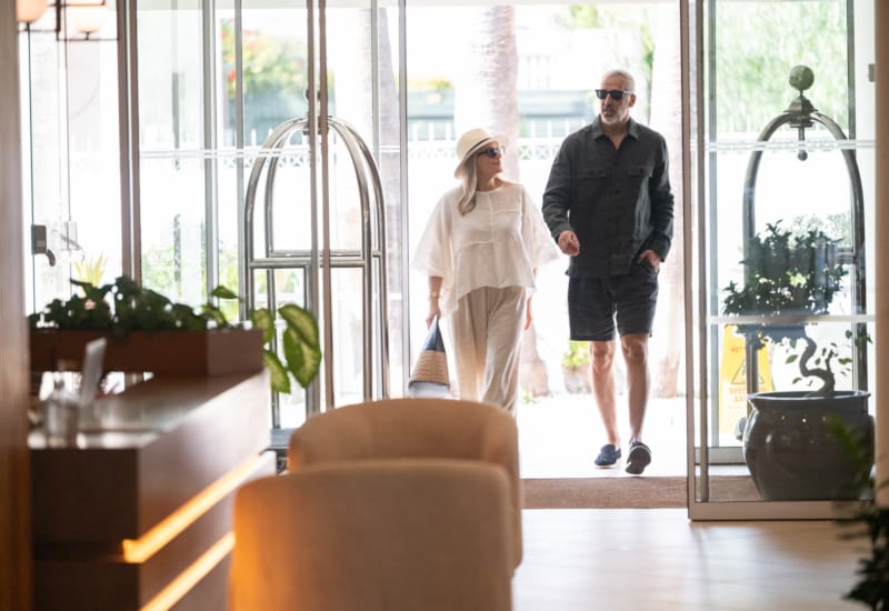 a man and woman walking in a room with windows and plants