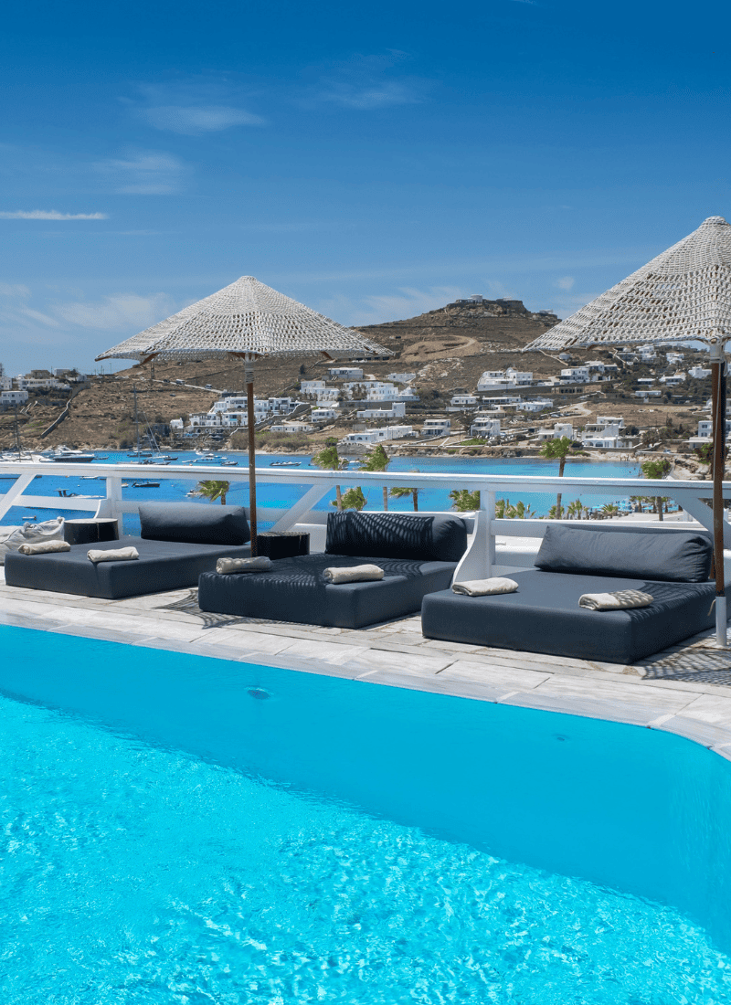 a pool with a lounge chair and a covered area with a building in the background