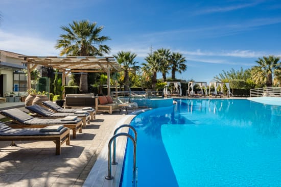 a pool with lounge chairs and a building with palm trees in the background