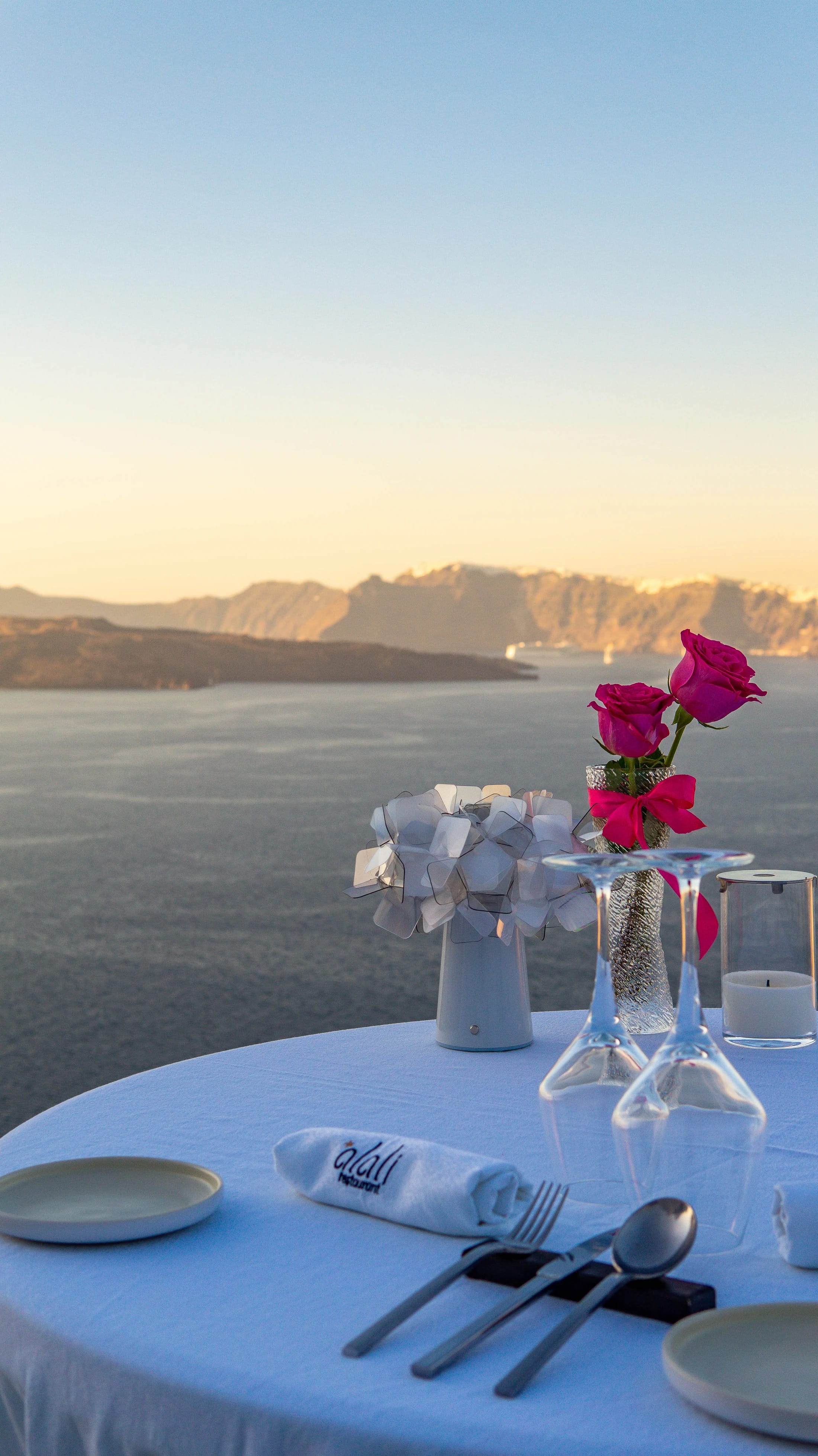a table with flowers and glasses on it by a body of water