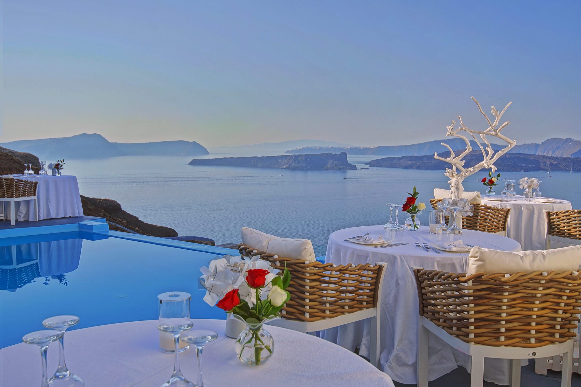 a table with chairs and a table with flowers on it by a body of water