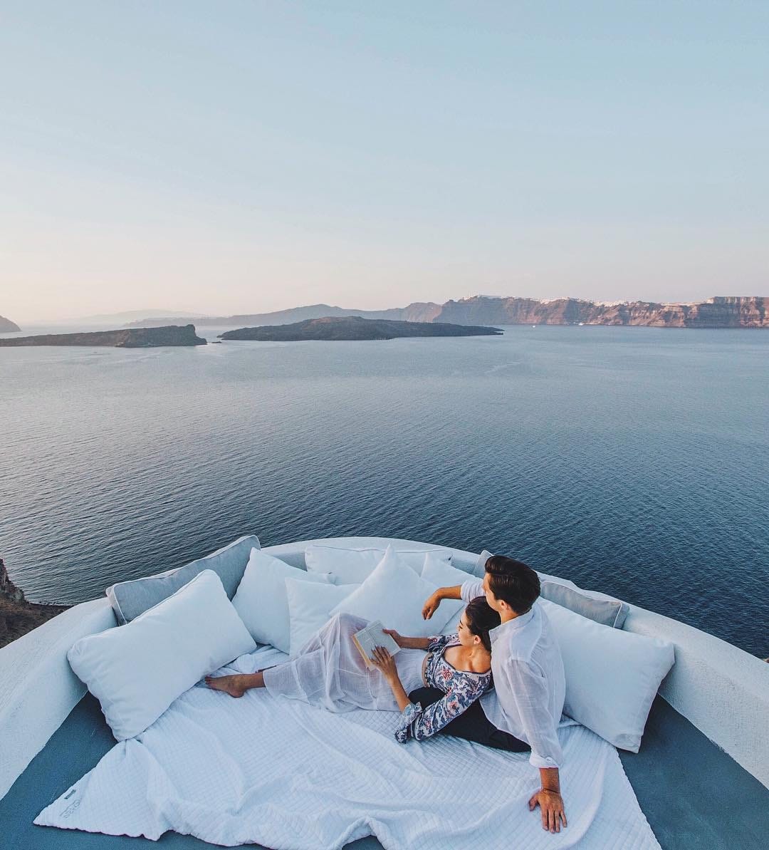 a man and woman lying on a bed with a body of water in the background