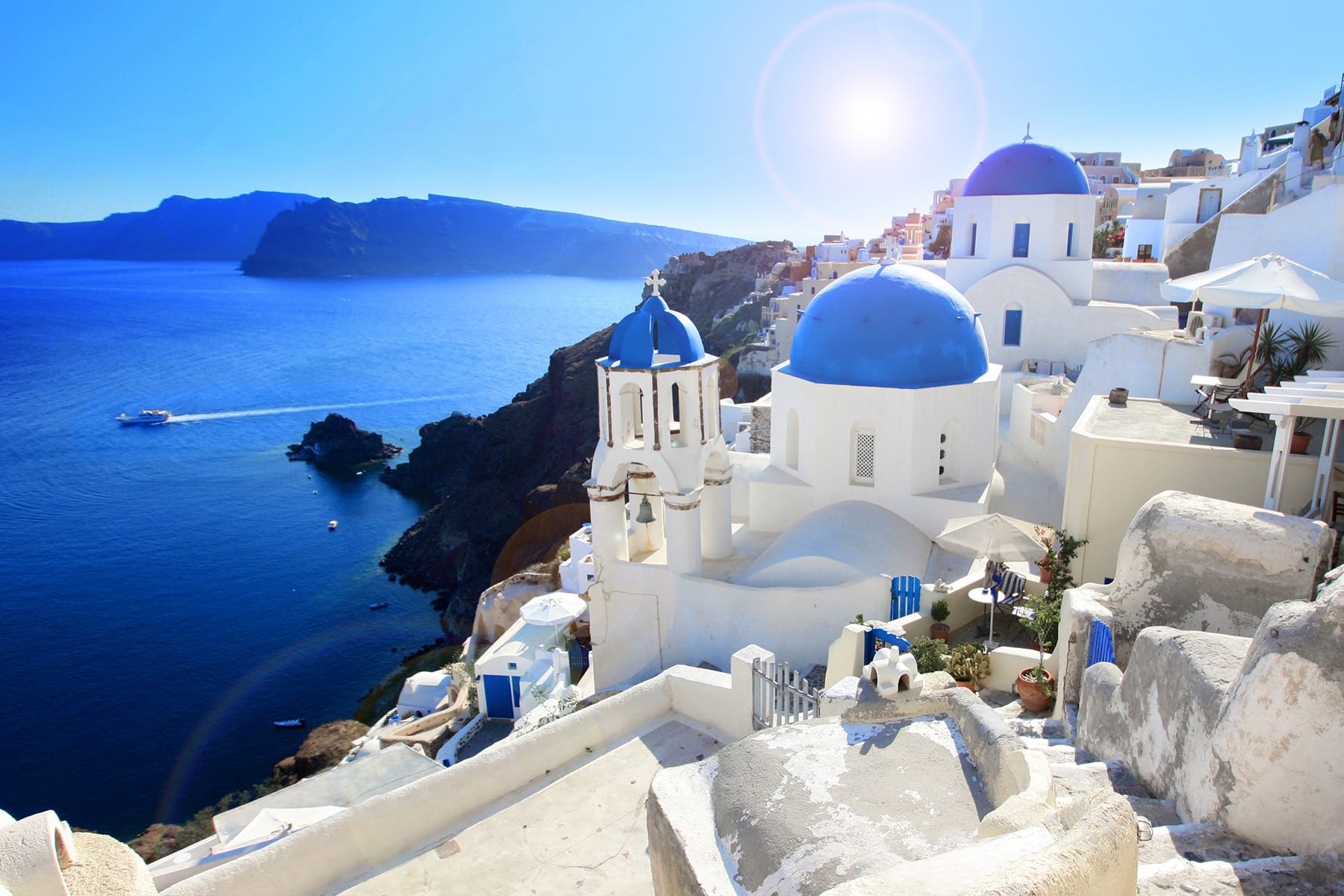 a white building on a rocky cliff with Santorini in the background