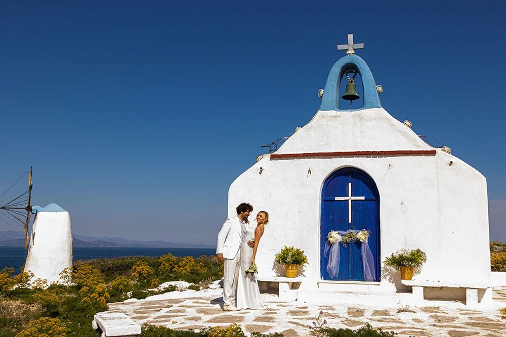 a couple of people standing in front of a white building with a blue door and a cross on