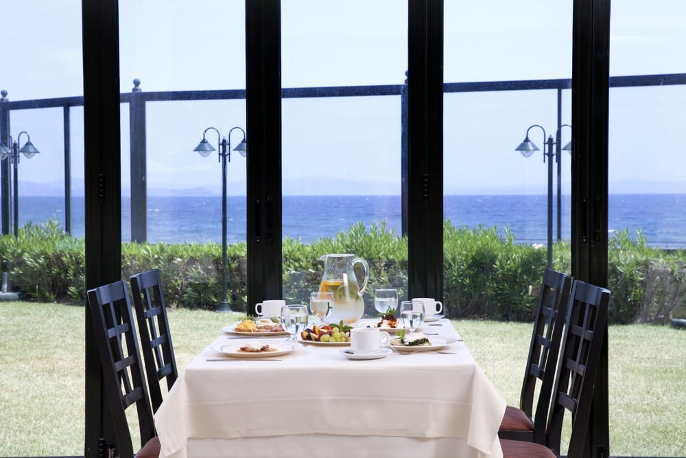 a table with plates and glasses on it by a window with a view of the ocean