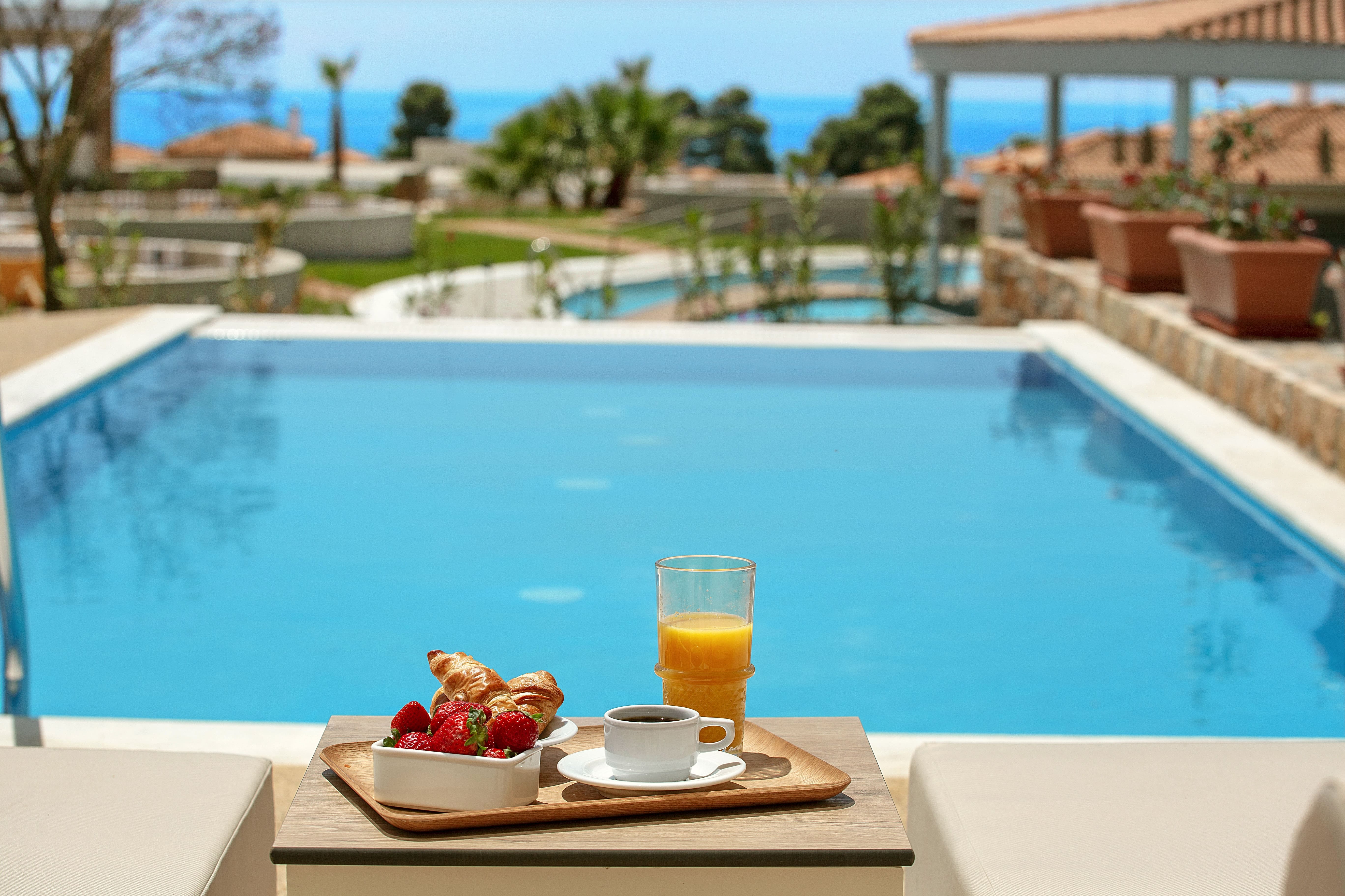 a tray of breakfast and a glass of juice next to a swimming pool
