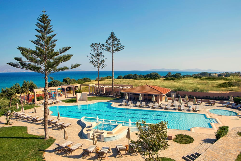 a pool with lounge chairs and palm trees by a beach