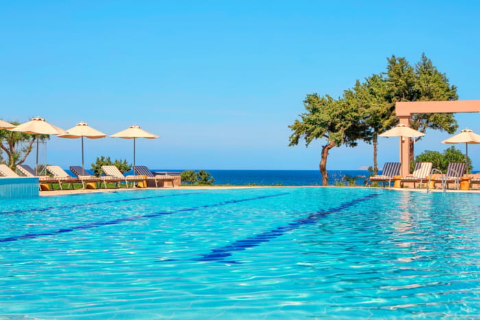 a pool with chairs and umbrellas by a beach