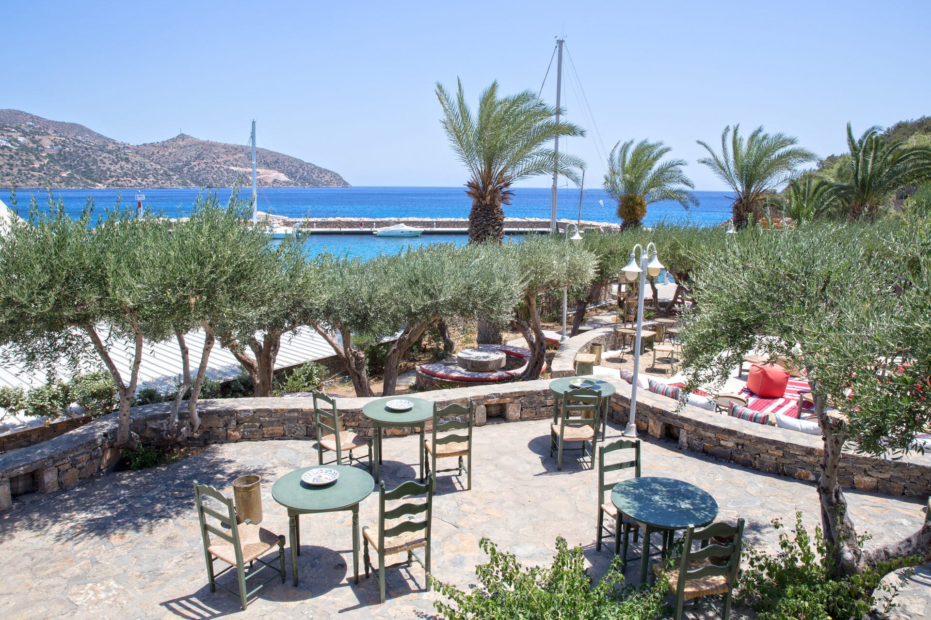 a patio with tables and chairs and trees by a body of water