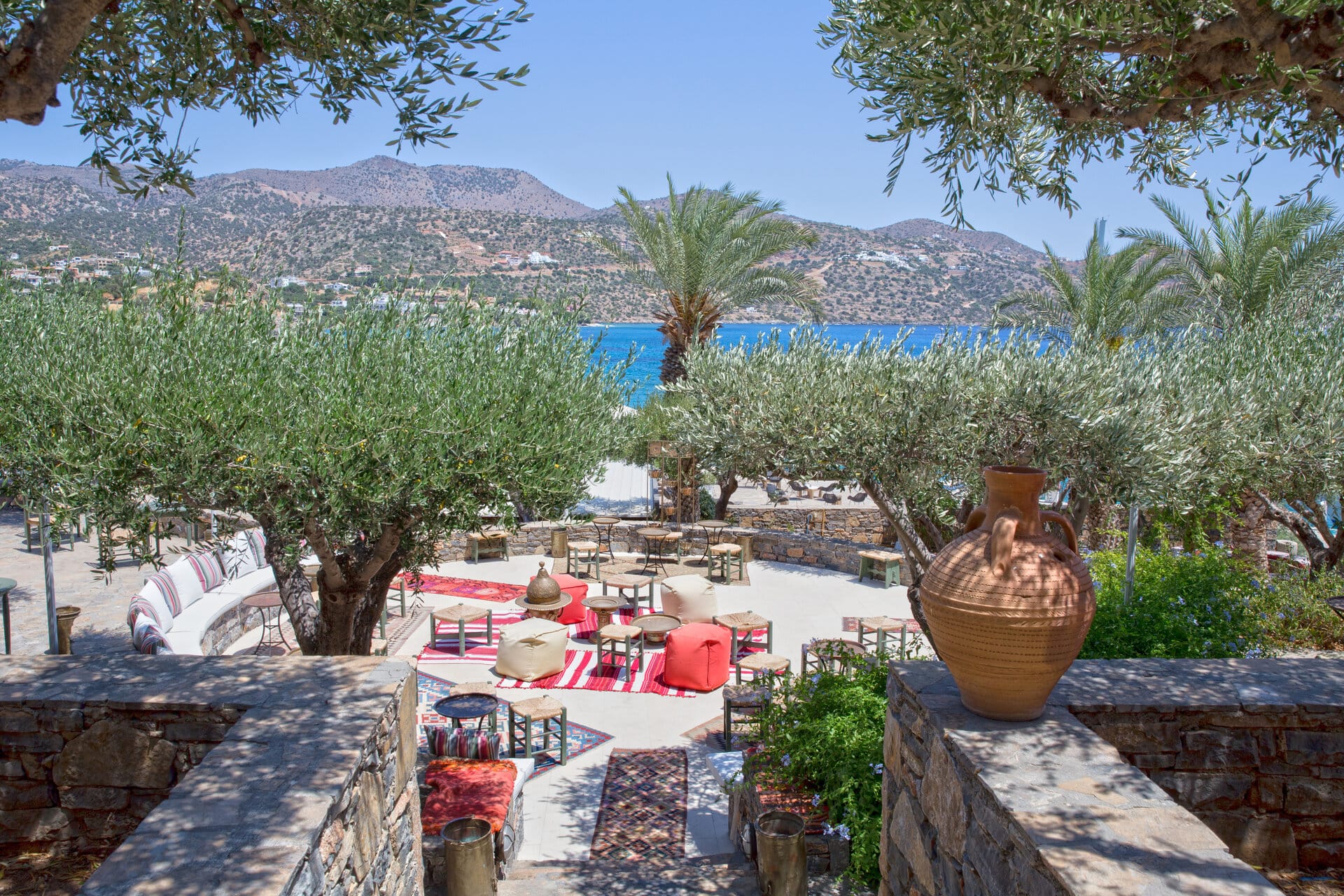 a patio with chairs and tables and trees with a body of water in the background